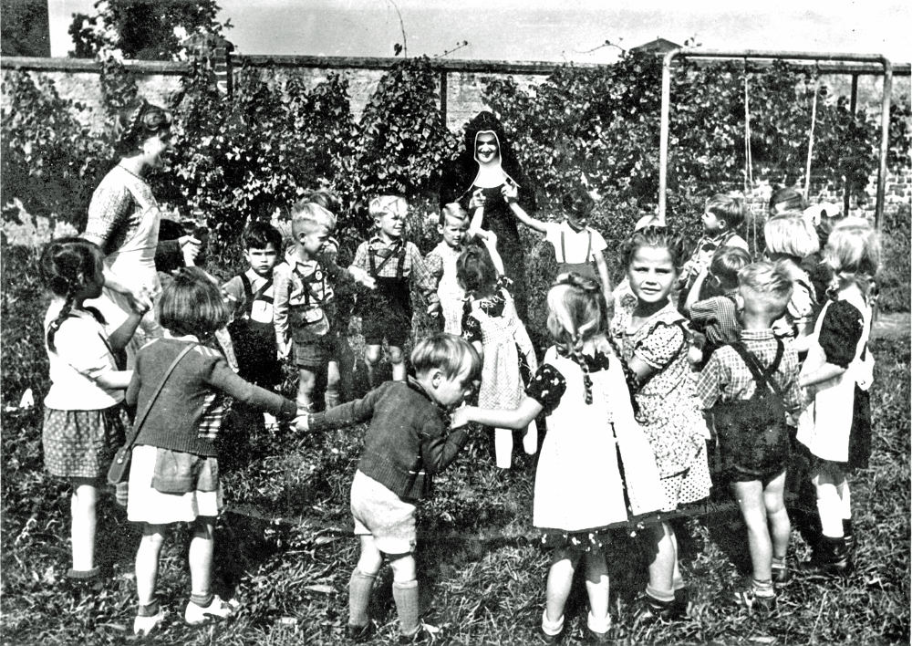 Gruppe singender Kinder mit Gruppenleiterinnen im katholischen Kindergarten um 1952 (Foto: Stadt Sankt Augustin / Sammlung Hedwig Bergfelder).